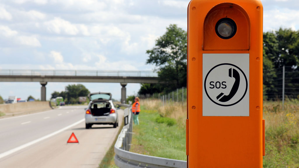 Borne d'appel d'urgence orange sur bande d'arrêt d'urgence avec véhicule immobilisé en arrière-plan